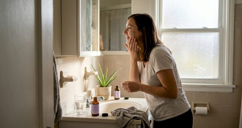 Woman applying botanical cream in sunlit bathroom