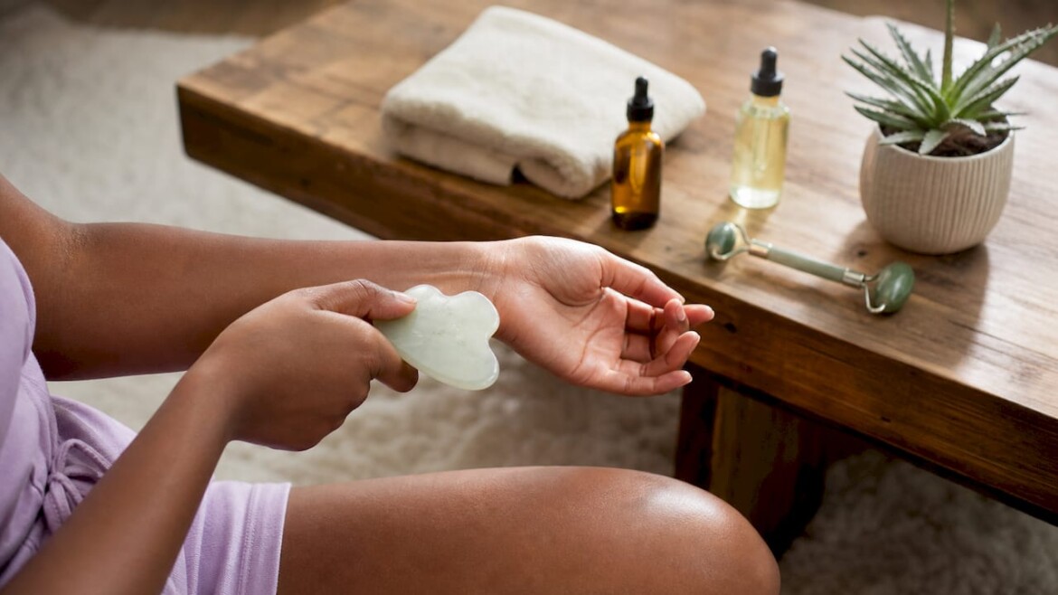 Hands holding gua sha stone over forearm in bathroom