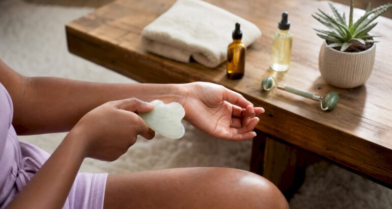 Hands holding gua sha stone over forearm in bathroom