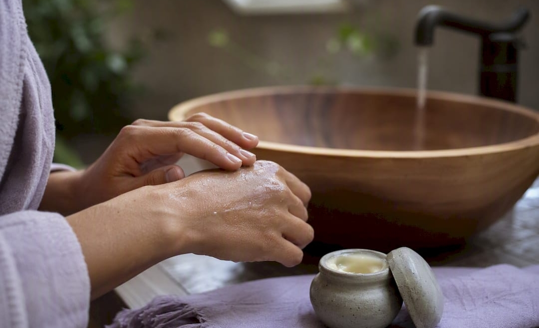 Hands applying balm to dry skin after washing