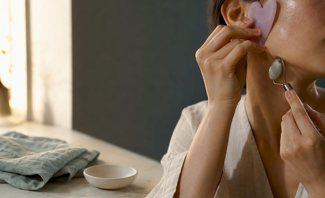 Hands using facial massage tools at vanity