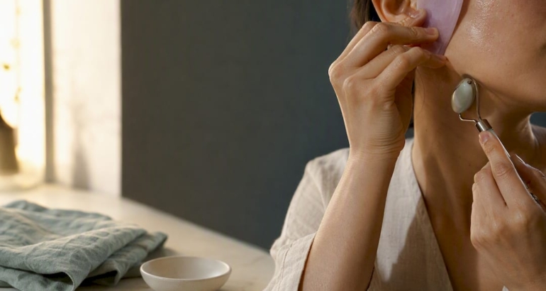 Hands using facial massage tools at vanity
